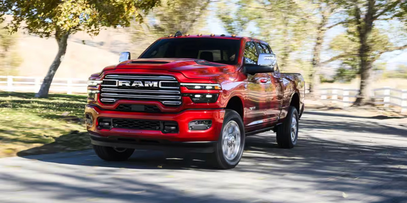 A red 2026 RAM 2500 driving on a tree-lined road