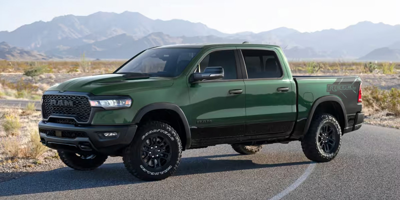 Green RAM 1500 Rebel parked on an asphalt road with desert mountains in the background.