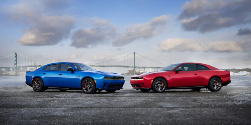 Blue and red muscle cars parked on wet pavement with a bridge in the background.